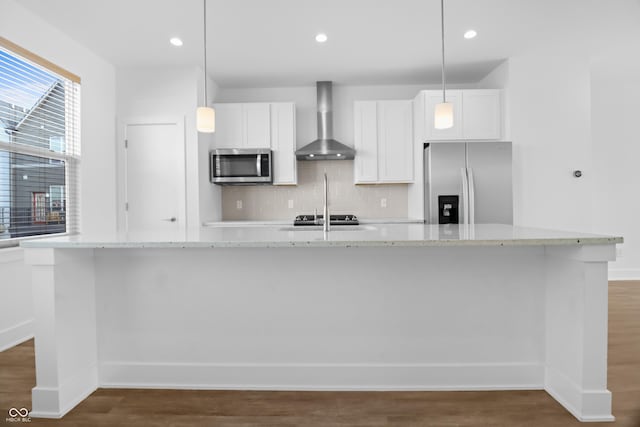 kitchen featuring a kitchen island with sink, white cabinets, hanging light fixtures, wall chimney exhaust hood, and stainless steel appliances