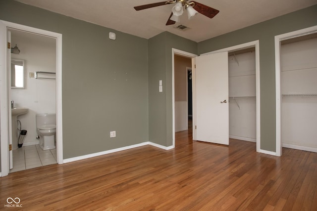 unfurnished bedroom featuring ensuite bath, ceiling fan, light hardwood / wood-style flooring, and multiple closets