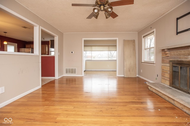 unfurnished living room with a stone fireplace, ceiling fan, light hardwood / wood-style floors, and a textured ceiling