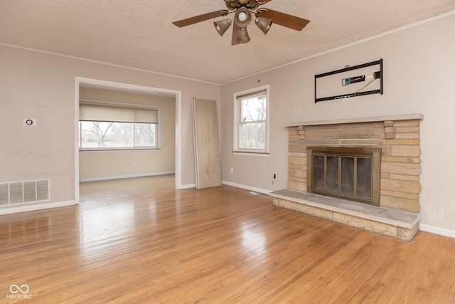 unfurnished living room with ceiling fan, ornamental molding, a fireplace, a textured ceiling, and light hardwood / wood-style floors