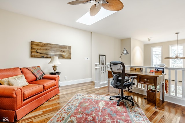 office area with ceiling fan, a skylight, and light hardwood / wood-style floors