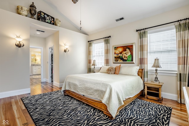 bedroom featuring ensuite bath, light wood-type flooring, and vaulted ceiling