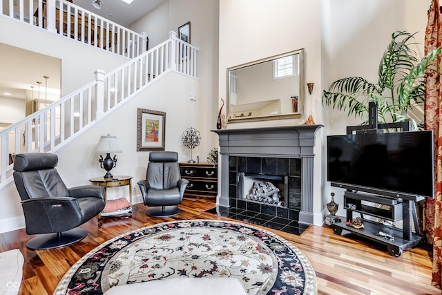 living room with a high ceiling, a tile fireplace, and wood-type flooring