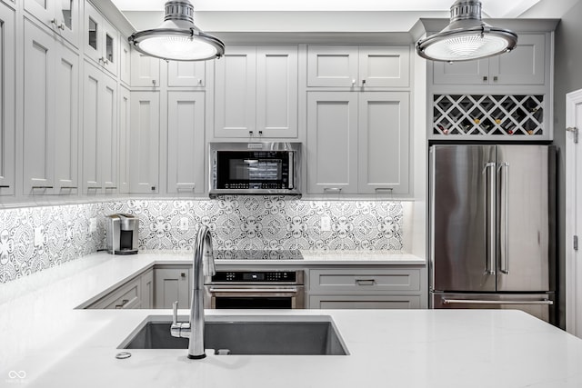 kitchen with stainless steel appliances, sink, backsplash, hanging light fixtures, and light stone countertops