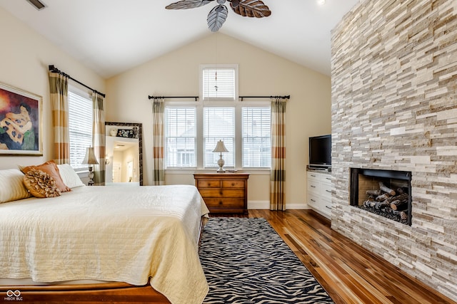 bedroom with ceiling fan, light hardwood / wood-style floors, a stone fireplace, and vaulted ceiling