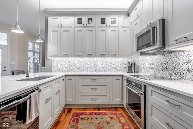 kitchen featuring pendant lighting, stainless steel appliances, decorative backsplash, light wood-type flooring, and sink