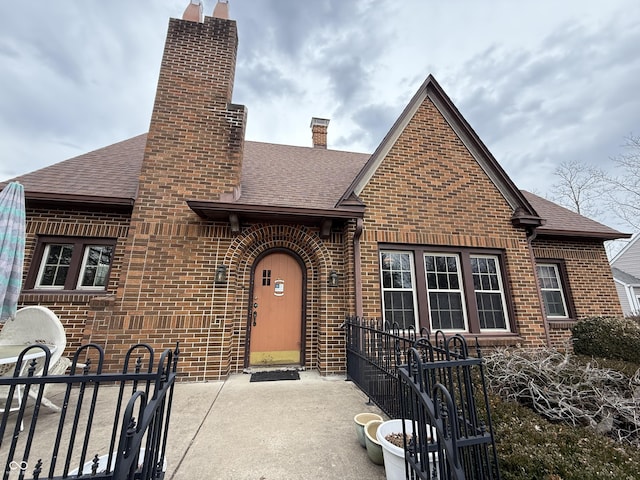 view of front facade with roof with shingles, a chimney, and brick siding