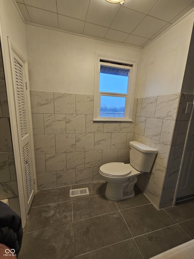 bathroom featuring toilet, tile patterned flooring, and tile walls