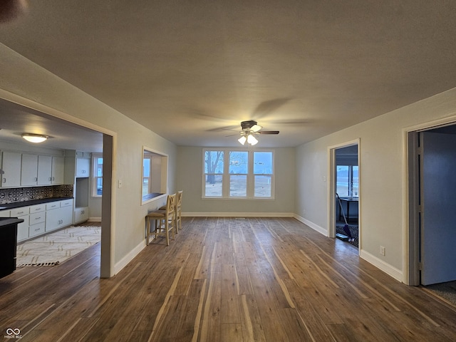 unfurnished living room featuring dark wood-type flooring and ceiling fan