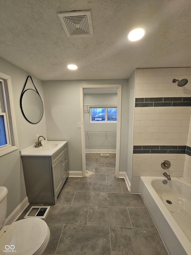 full bathroom featuring vanity, toilet, tiled shower / bath combo, and a textured ceiling