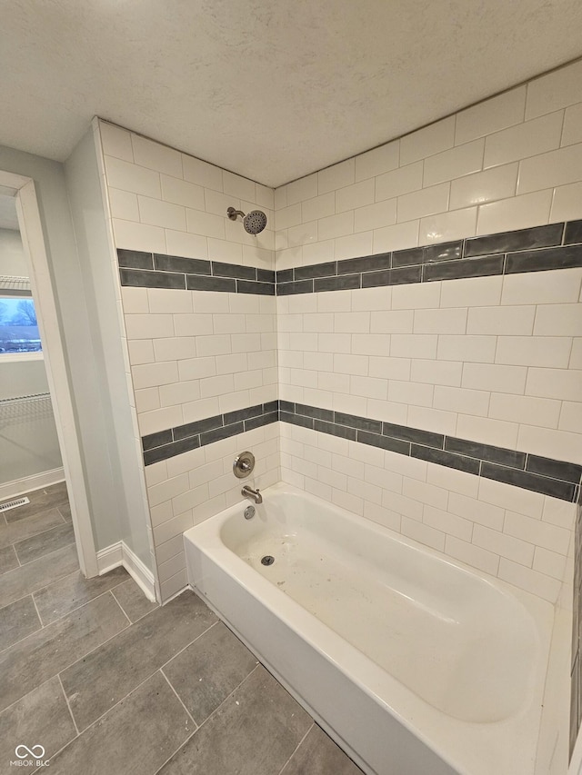 bathroom with a textured ceiling and tiled shower / bath