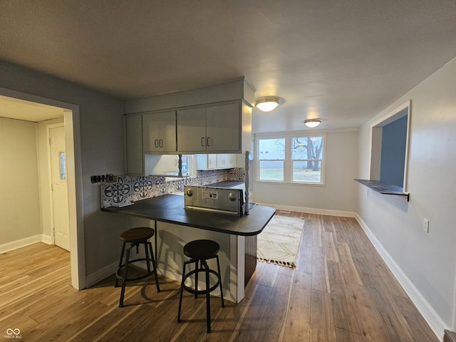 kitchen with a breakfast bar area, gray cabinetry, tasteful backsplash, kitchen peninsula, and light hardwood / wood-style floors