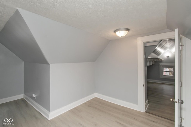 additional living space featuring a textured ceiling, light hardwood / wood-style flooring, and lofted ceiling