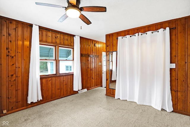 carpeted spare room featuring ceiling fan and wood walls