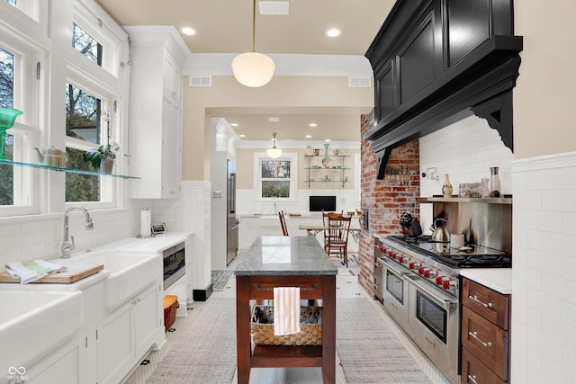 kitchen featuring a center island, sink, light stone counters, double oven range, and decorative light fixtures