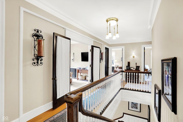 hallway with wood-type flooring, ornamental molding, and a notable chandelier