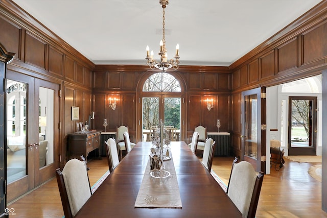 dining room with french doors, an inviting chandelier, and wooden walls