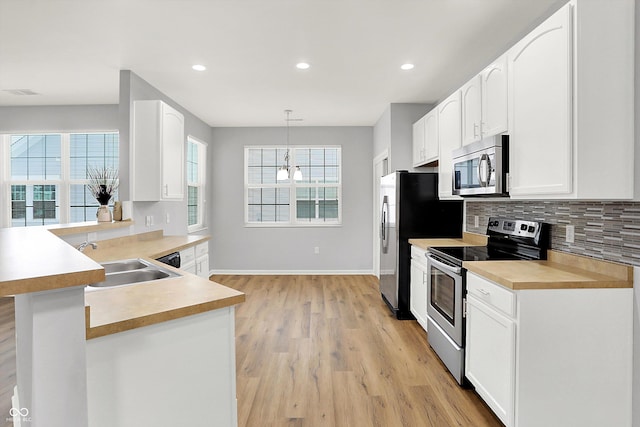 kitchen featuring kitchen peninsula, backsplash, stainless steel appliances, sink, and decorative light fixtures