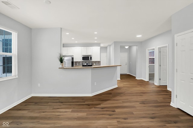 kitchen with kitchen peninsula, backsplash, stainless steel appliances, dark wood-type flooring, and white cabinetry