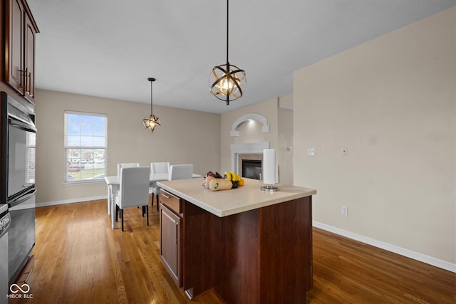 kitchen featuring dark wood-type flooring, hanging light fixtures, double oven, dark brown cabinets, and a kitchen island