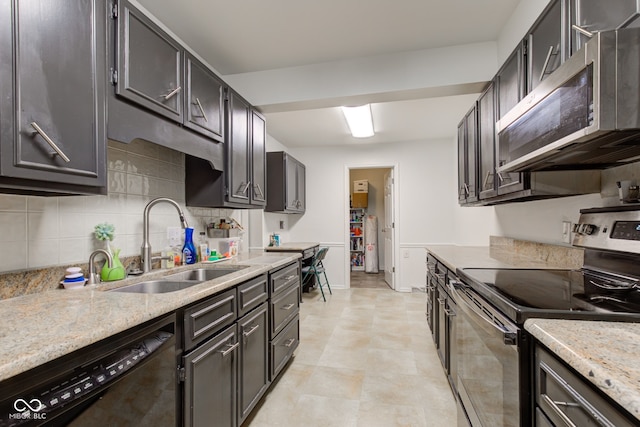 kitchen featuring backsplash, light stone countertops, sink, and appliances with stainless steel finishes