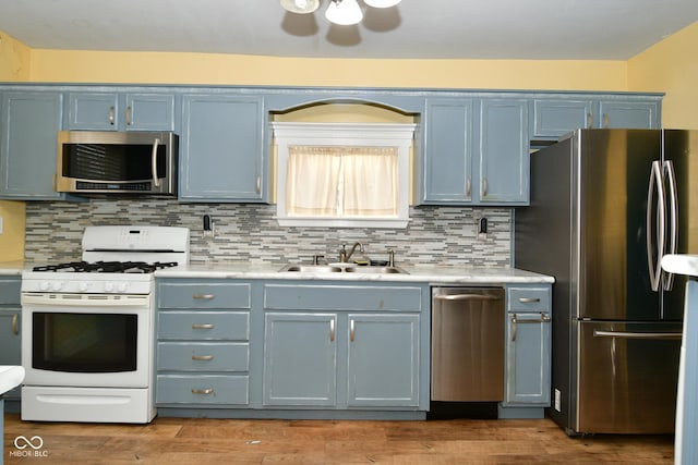 kitchen with backsplash, blue cabinets, sink, hardwood / wood-style flooring, and stainless steel appliances