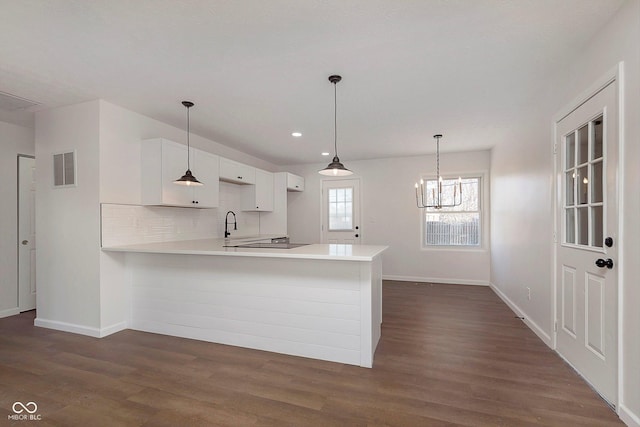 kitchen with pendant lighting, dark wood-type flooring, kitchen peninsula, tasteful backsplash, and white cabinetry