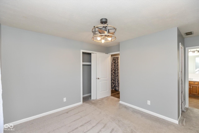 unfurnished bedroom featuring an inviting chandelier, light colored carpet, a textured ceiling, and a closet