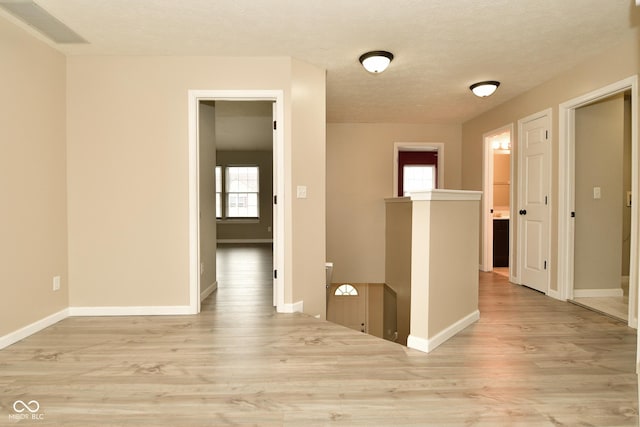 corridor featuring plenty of natural light, a textured ceiling, and light hardwood / wood-style flooring