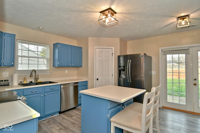 kitchen featuring blue cabinets, sink, appliances with stainless steel finishes, a kitchen island, and a kitchen bar