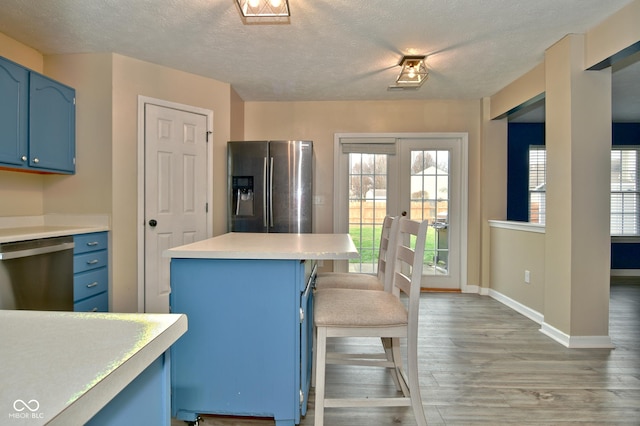 kitchen with appliances with stainless steel finishes, french doors, a breakfast bar, blue cabinetry, and light hardwood / wood-style floors