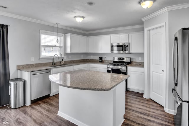 kitchen with appliances with stainless steel finishes, sink, pendant lighting, white cabinets, and a kitchen island