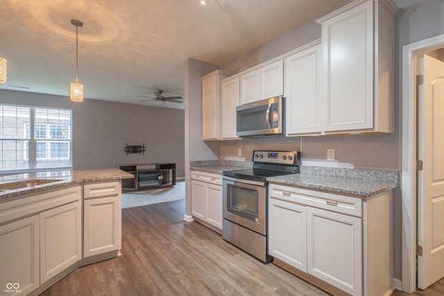 kitchen with ceiling fan, light stone counters, stainless steel appliances, light wood-type flooring, and pendant lighting