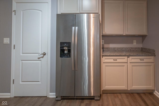 kitchen with light stone countertops, stainless steel fridge, baseboards, and wood finished floors