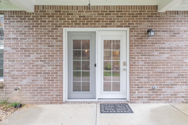 view of exterior entry featuring brick siding and a patio area