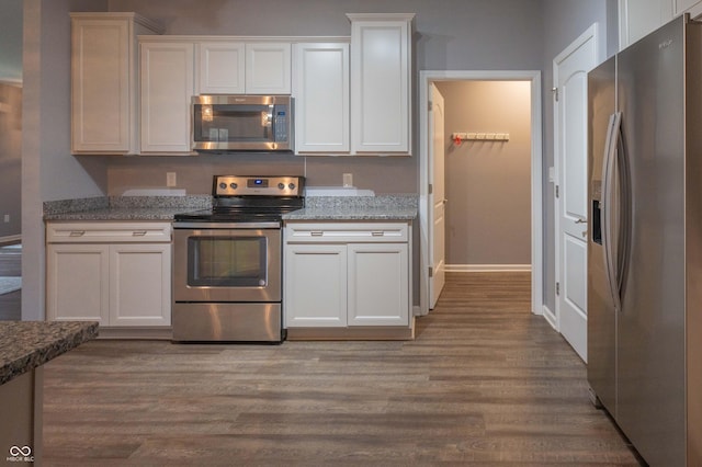 kitchen featuring baseboards, wood finished floors, light stone countertops, stainless steel appliances, and white cabinetry