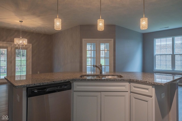 kitchen with stainless steel dishwasher, stone countertops, open floor plan, white cabinets, and a sink