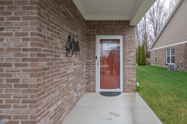 view of exterior entry with a yard, cooling unit, and brick siding