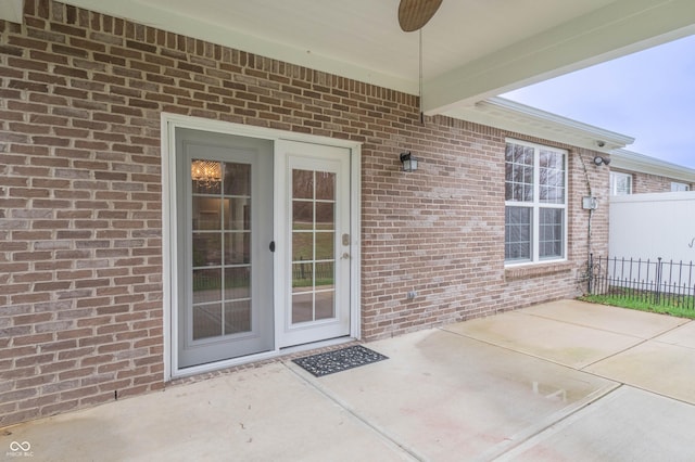 doorway to property with a patio area, brick siding, fence, and ceiling fan