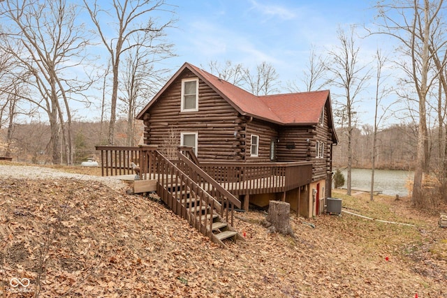 view of front of house featuring a wooden deck, central air condition unit, log exterior, and a wooded view