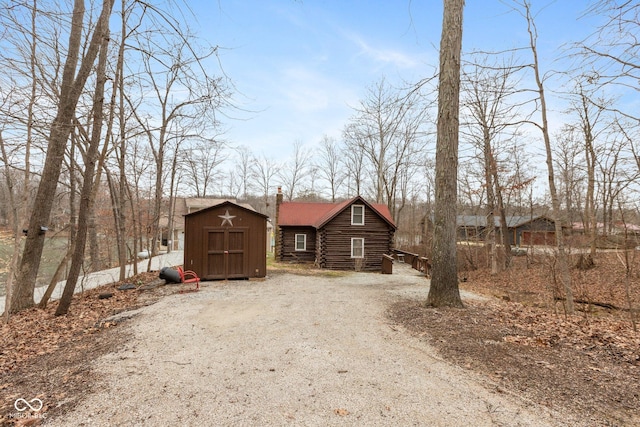 view of front of home with driveway, log siding, a chimney, an outdoor structure, and a storage unit