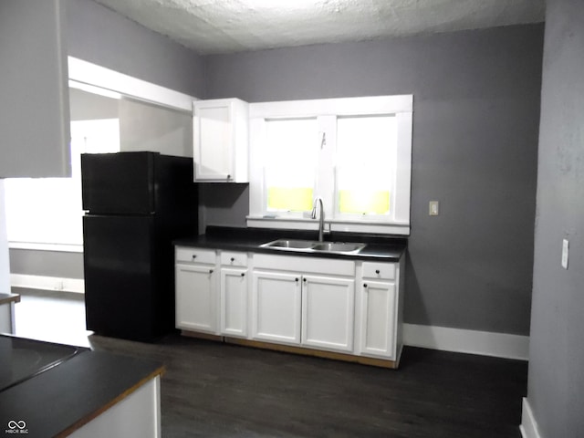 kitchen featuring a textured ceiling, black refrigerator, white cabinetry, and sink