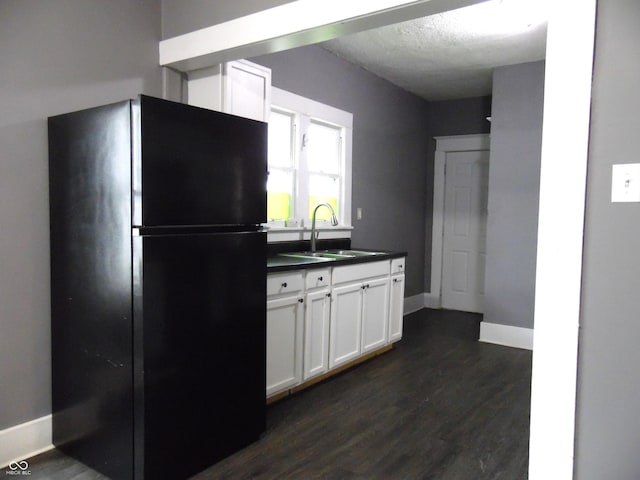 kitchen featuring dark wood-type flooring, white cabinets, black fridge, sink, and a textured ceiling