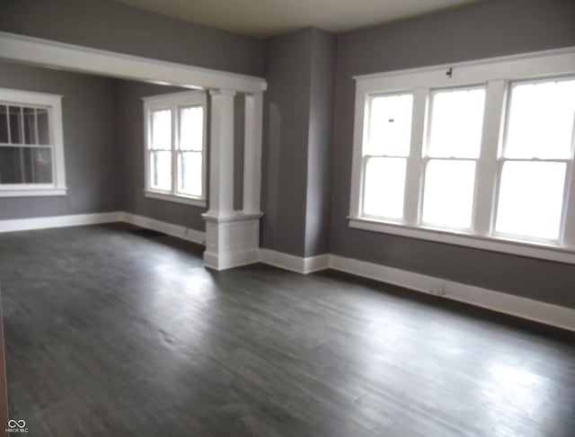 spare room featuring dark hardwood / wood-style flooring and decorative columns