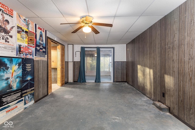 interior space with a paneled ceiling, wooden walls, and concrete floors