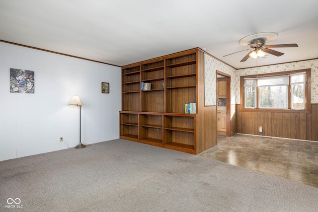 unfurnished living room featuring carpet, ceiling fan, wood walls, and ornamental molding