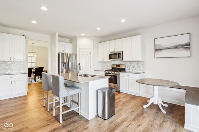 kitchen with a kitchen island with sink, white cabinets, sink, light hardwood / wood-style flooring, and appliances with stainless steel finishes