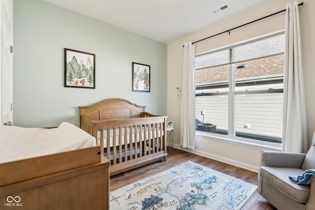 bedroom with wood-type flooring, a crib, and multiple windows