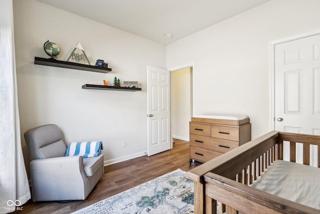 bedroom with a crib and dark wood-type flooring