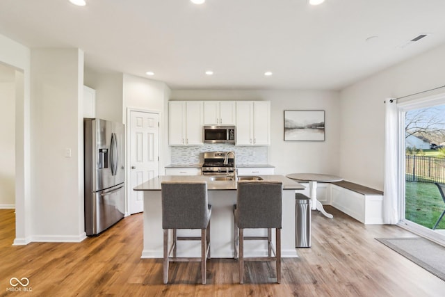 kitchen with tasteful backsplash, an island with sink, a kitchen bar, white cabinets, and appliances with stainless steel finishes